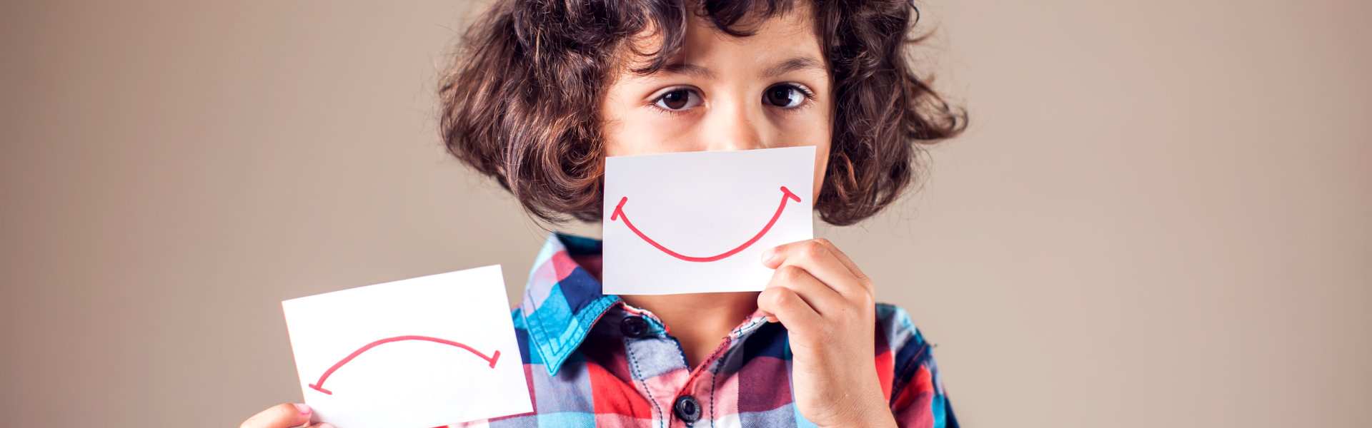 child with a smiley drawing paper in the face
