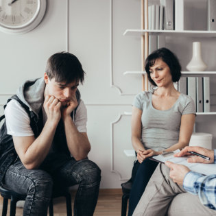 teenager sits next to his mother during a meeting with therapists
